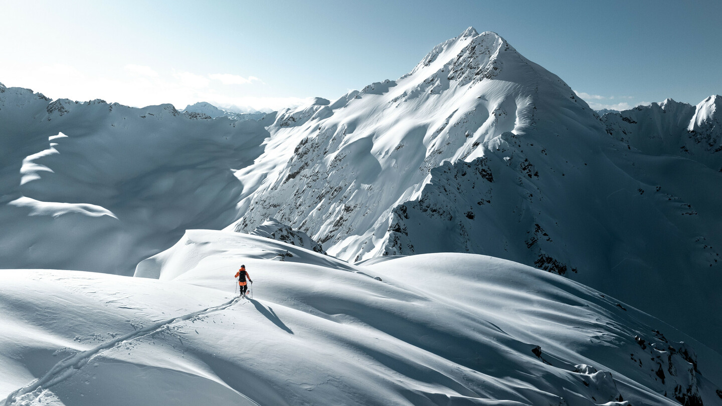 A skier on a snowy mountain landscape under bright sunshine, surrounded by majestic peaks and untouched snow.